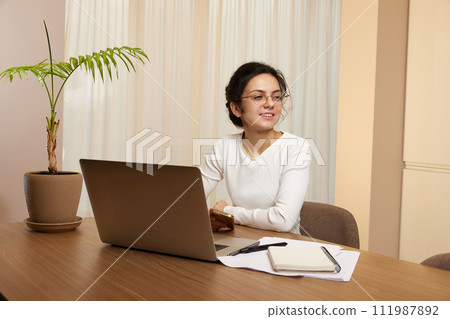 pretty woman in glasses using laptop and communicates with customer on internet at home 111987892