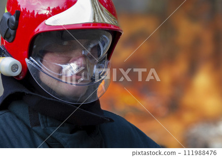 The face of a fireman in a helmet on a background of fire. Putting out a fire. 111988476
