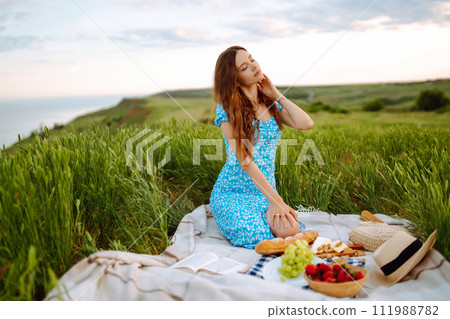 Young woman sits on a plaid with a book. Summer picnic in nature. Healthy food. 111988782