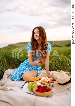 Young woman sits on a plaid with a book. Summer picnic in nature. Healthy food. 111988807