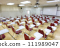 Blurred abstract background of examination room with undergraduate students inside. Blurred view of a student doing the final test in the exam room. Blurry view of study chairs in university. 111989047
