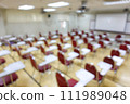 Blurred abstract background of examination room with undergraduate students inside. Blurred view of a student doing the final test in the exam room. Blurry view of study chairs in university. 111989048