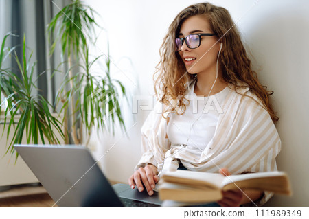 Young woman sits at home, learning preparing for exam using literature laptop, concept of knowledge. Young woman sits at home, learning preparing for exam using literature laptop, concept of knowledge. 111989349