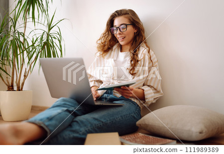 Young woman sits at home, learning preparing for exam using literature laptop, concept of knowledge. Young woman sits at home, learning preparing for exam using literature laptop, concept of knowledge. 111989389