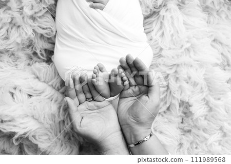 The palms of the father, the mother are holding the foot of the newborn baby. Feet of the newborn on the palms of the parents. Studio macro black and white photo of a child's toes, heels and feet. The palms of the father, the mother are holding the foot of the newborn baby. Feet of the newborn on the palms of the parents. Studio macro black and white photo of a child's toes, heels and feet. 111989568