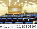 blurred or defocused people in the seminar convention hall. Business meeting for a press conference or lecturer education concept with a wide view from the room's corner. Modern, blurry auditorium. 111989596