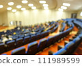 blurred or defocused people in the seminar convention hall. Business meeting for a press conference or lecturer education concept with a wide view from the room's corner. Modern, blurry auditorium. 111989599