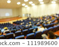 blurred or defocused people in the seminar convention hall. Business meeting for a press conference or lecturer education concept with a wide view from the room's corner. Modern, blurry auditorium. 111989600