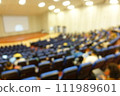blurred or defocused people in the seminar convention hall. Business meeting for a press conference or lecturer education concept with a wide view from the room's corner. Modern, blurry auditorium. 111989601