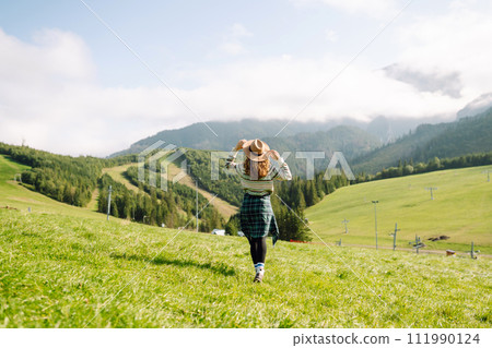 Woman walking on through green grass valley on background big mountains. Resting concept. 111990124