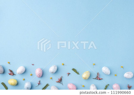 Festive Easter background. Multicoloured Easter eggs and flowers on a blue table. Card with a place for text. Top view. Festive Easter background. Multicoloured Easter eggs and flowers on a blue table. Card with a place for text. Top view. 111990660