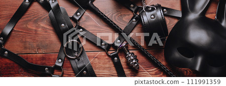 set of BDSM sex toys with handcuffs, whip flogger, butt anal plug for submission and domination on wooden background 111991359