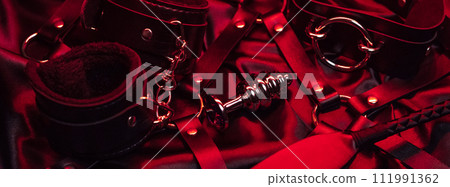 set of BDSM sex toys with handcuffs, whip flogger, butt anal plug for submission and domination on red background set of BDSM sex toys with handcuffs, whip flogger, butt anal plug for submission and domination on red background 111991362