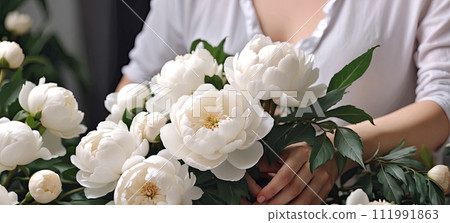 A female florist collects a bouquet of pions- fresh cut flowers in boxes and vases in a warehouse and racks for sale, delivery for the holiday. Spring, March 8, women's Day, birthday. AI generated 111991863