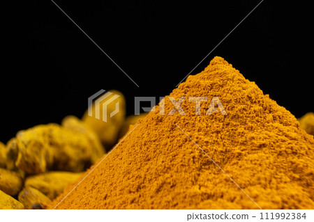 Turmeric powder and dried turmeric root on a black background 111992384