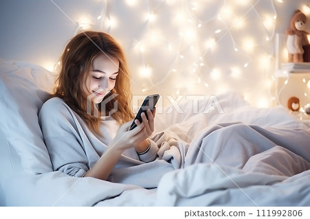 AI-generated content. A teenage girl sits in bed in a bedroom decorated with Christmas decor and looks at a mobile phone or tablet. 111992806