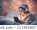 AI-generated content. A teenage girl wearing headphones sits in bed in a bedroom decorated with Christmas decor and looks at a mobile phone or tablet. 111992807