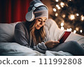 AI-generated content. A teenage girl wearing headphones sits in bed in a bedroom decorated with Christmas decor and looks at a mobile phone or tablet. 111992808