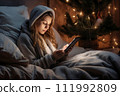AI-generated content. Lonely young woman sitting in bed in a bedroom decorated with Christmas decor and looking at a mobile phone or tablet 111992809
