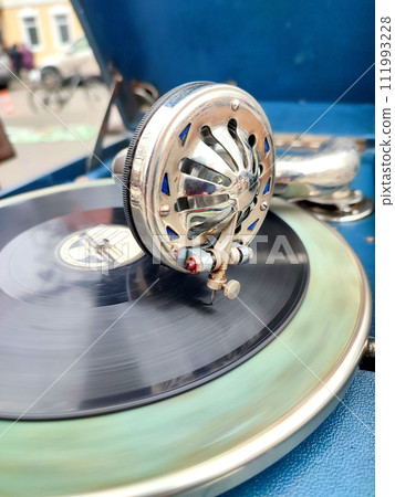 An old retro record playing on old vintage gramophone at flea market. Work of portable gramophone. Old vintage shabby record player, phonograph, potefone. Needle close up. Nostalgia antique turntable An old retro record playing on old vintage gramophone at flea market. Work of portable gramophone. Old vintage shabby record player, phonograph, potefone. Needle close up. Nostalgia antique turntable 111993228