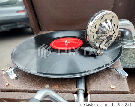 An old retro record playing on old vintage gramophone at flea market. Work of portable gramophone. Old vintage shabby record player, phonograph, potefone. Needle close up. Nostalgia antique turntable An old retro record playing on old vintage gramophone at flea market. Work of portable gramophone. Old vintage shabby record player, phonograph, potefone. Needle close up. Nostalgia antique turntable 111993231