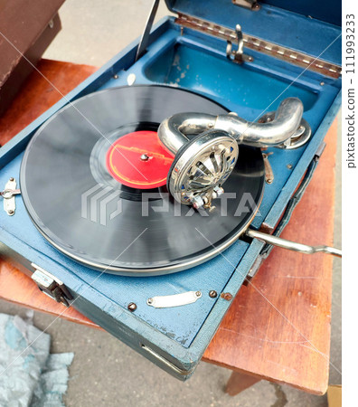 An old retro record playing on old vintage gramophone at flea market. Work of portable gramophone. Old vintage shabby record player, phonograph, potefone. Needle. Nostalgia antique audio turntable An old retro record playing on old vintage gramophone at flea market. Work of portable gramophone. Old vintage shabby record player, phonograph, potefone. Needle. Nostalgia antique audio turntable 111993233