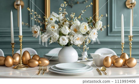 Festive Easter set table with white ceramic plates, ceramic golden eggs, golden forks and knives, flowers 111993406