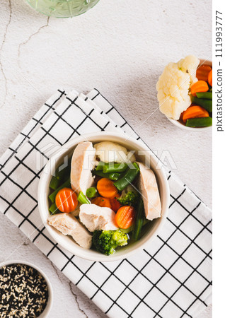Diet soup with chicken fillet and boiled vegetables in a bowl on the table top and vertical view Diet soup with chicken fillet and boiled vegetables in a bowl on the table top and vertical view 111993777