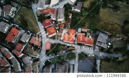 This aerial view showcases a city nestled amidst towering mountains in the background. The cityscape is dotted with buildings, roads, and green spaces, while the majestic mountains provide a stunning 111994386