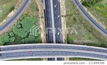 An overhead perspective of a highway featuring two lanes for vehicles to travel. The road stretches into the distance, with cars and trucks moving in different directions. 111994398