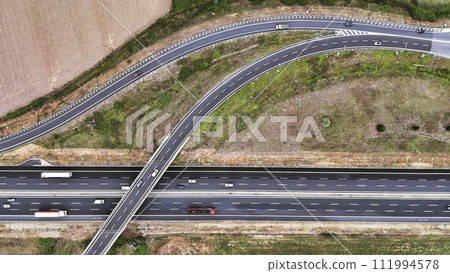 An overhead perspective of a highway featuring two lanes for vehicles to travel. The road stretches into the distance, with cars and trucks moving in different directions. An overhead perspective of a highway featuring two lanes for vehicles to travel. The road stretches into the distance, with cars and trucks moving in different directions. 111994578