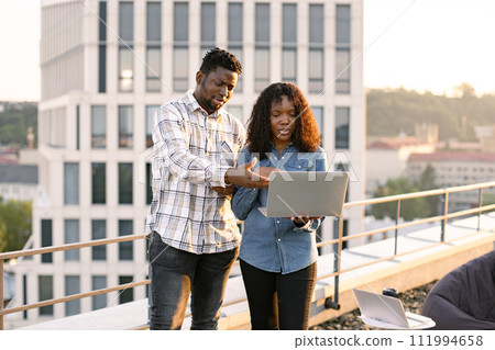Two African American business people outdoors during break standing on rooftop. 111994658