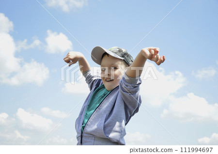 handsome boy in a cap against a background of blue sky with white clouds 111994697