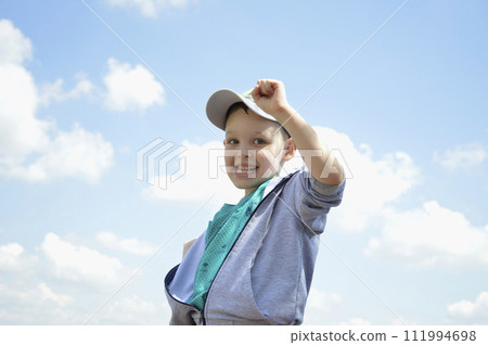 handsome boy in a cap against a background of blue sky with white clouds 111994698
