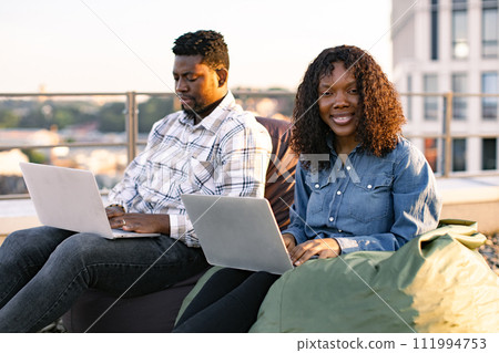 African colleagues working with laptops while sitting at beanbags. African colleagues working with laptops while sitting at beanbags. 111994753