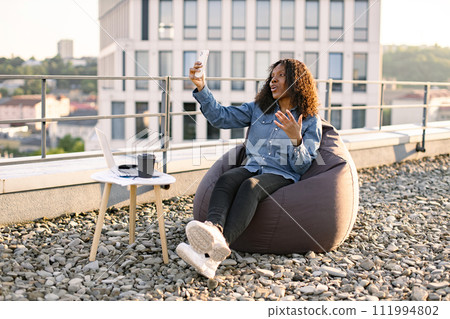 African woman in casual shirt using phone while recording video for her vlog. 111994802