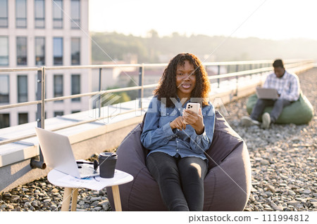 African American person with smartphone resting in pouf chair . African American person with smartphone resting in pouf chair . 111994812