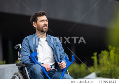 Bearded young man with sticks on a wheelchair Bearded young man with sticks on a wheelchair 111994831