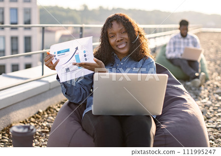 African businesswoman in headset discussing financial plan looking at camera. 111995247