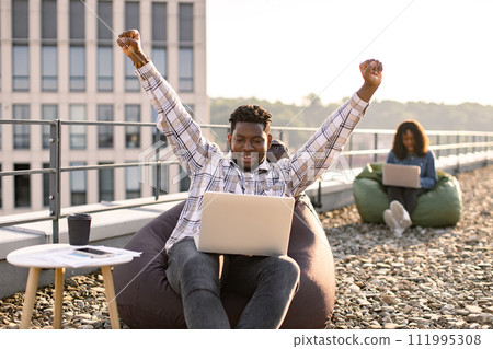 African American man screaming and raising hand up looking at laptop. 111995308