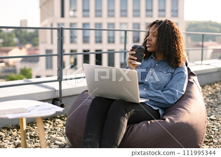 African female drinking coffee while sitting on bean bag chair. African female drinking coffee while sitting on bean bag chair. 111995344