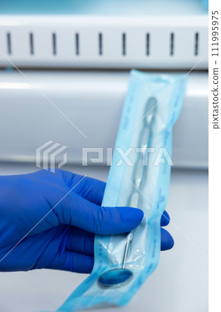 Dentist hands in blue gloves holding dentist tools doing sterilization of instruments Dentist hands in blue gloves holding dentist tools doing sterilization of instruments 111995975