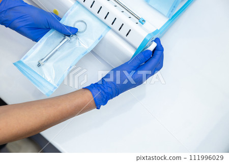 Dentist hands in blue gloves holding dentist tools using sterilizing box 111996029