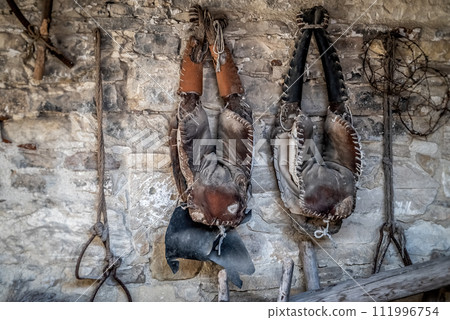 Old worn saddle hanging from an old barn stone wall Old worn saddle hanging from an old barn stone wall 111996754