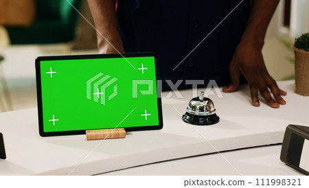 Tourist asking about greenscreen display, pointing at digital tablet on reception front desk in hotel lobby. Female employee explaining about blank mockup copyspace template, tourism. Tourist asking about greenscreen display, pointing at digital tablet on reception front desk in hotel lobby. Female employee explaining about blank mockup copyspace template, tourism. 111998321
