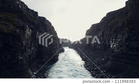 Aerial view of majestic waterfall in iceland, river flow running down off hills wih frozen fields and landscapes. Fantastic icelandic nature with water stream flowing, canyon rocks. Slow motion. Aerial view of majestic waterfall in iceland, river flow running down off hills wih frozen fields and landscapes. Fantastic icelandic nature with water stream flowing, canyon rocks. Slow motion. 111998383