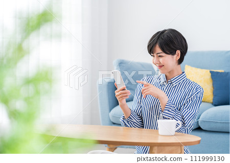 A woman who operates a smartphone in the living room. 111999130