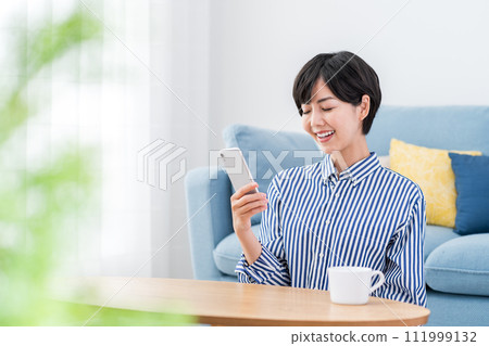 一個在客廳裡操作智能手機的女人。 111999132