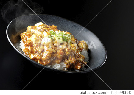 一張黑色背景下滾燙的麻婆碗的照片，上面放著大量的豆腐和蔥 111999398