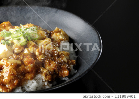 一張黑色背景下滾燙的麻婆碗的照片，上面放著大量的豆腐和蔥 111999401
